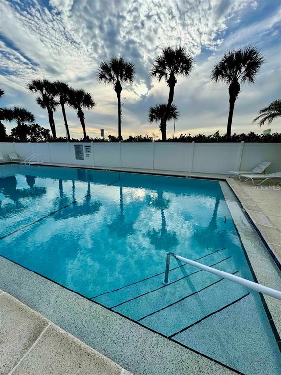 A swimming pool with steps and a handrail is surrounded by a white fence and palm trees — 14459 RIVER BEACH DRIVE UNIT 129, PORT CHARLOTTE, FL