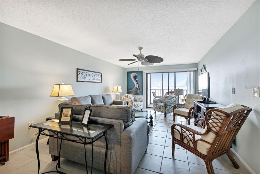 A living room features gray furniture, tile floors, a ceiling fan, and a balcony view — 14459 RIVER BEACH DRIVE UNIT 129, PORT CHARLOTTE, FL