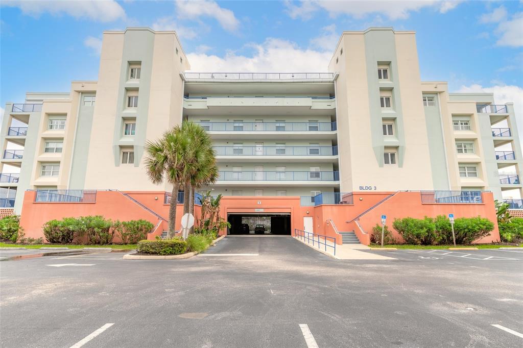 A multi-story apartment building with a central parking garage entrance and a palm tree — 5300 S ATLANTIC AVENUE UNIT 3-605, NEW SMYRNA BEACH, FL