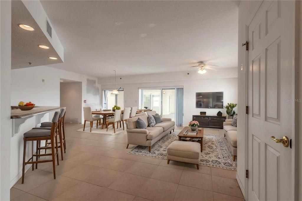 An open-concept living and dining area features tile flooring, neutral furniture, and a breakfast bar — 5300 S ATLANTIC AVENUE UNIT 3-605, NEW SMYRNA BEACH, FL