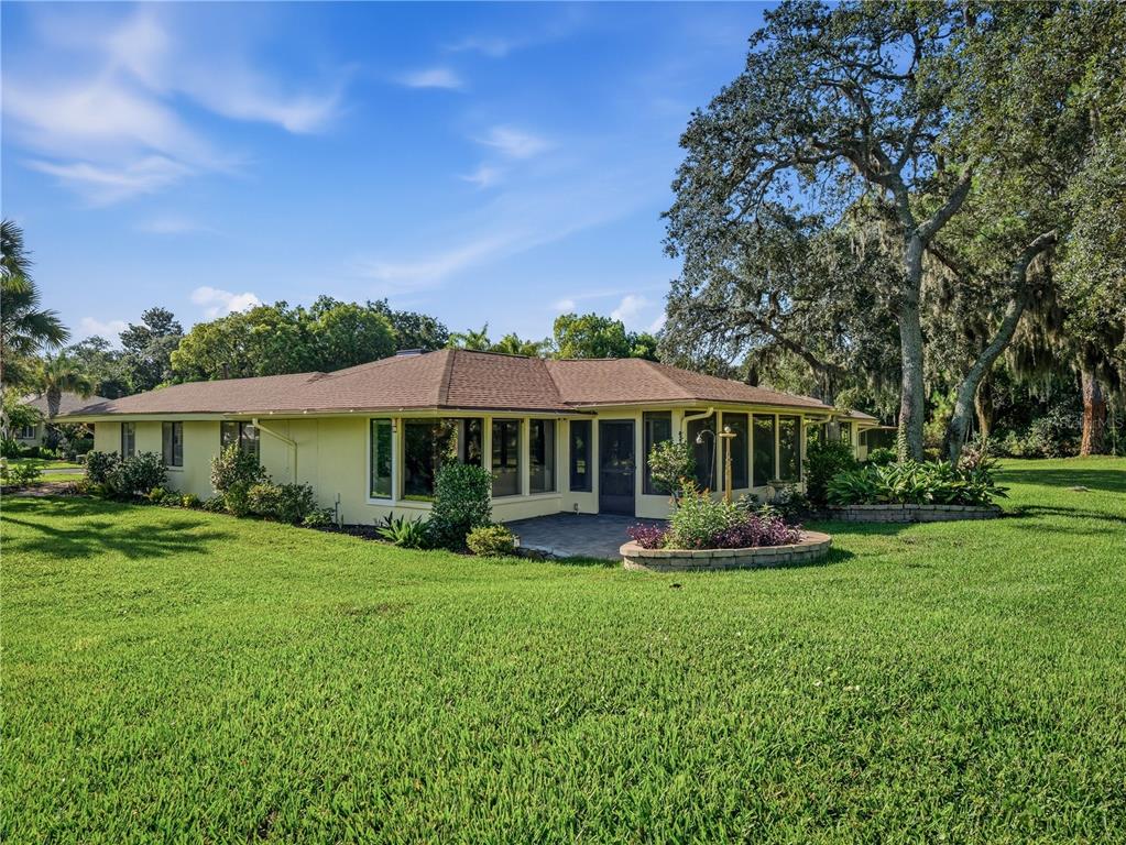 A yellow single-story house with a brown roof sits on a large, grassy lawn — 214 CANTERBURY CIRCLE, NEW SMYRNA BEACH, FL
