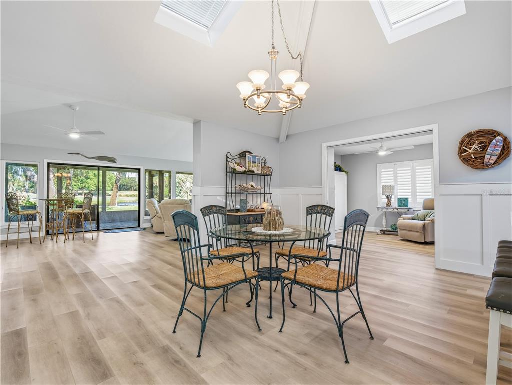 A dining area features a glass table, metal chairs, light wood flooring, and vaulted ceilings — 214 CANTERBURY CIRCLE, NEW SMYRNA BEACH, FL