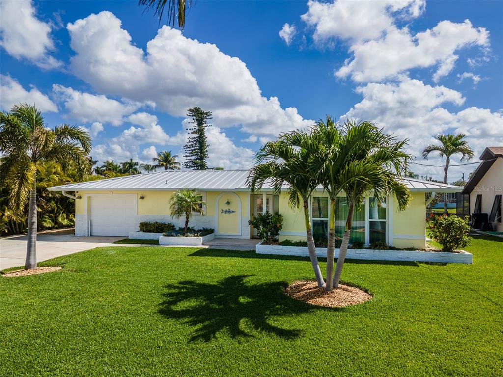 A yellow single-story house with a white metal roof features a front lawn and palms — 3517 SE 1ST AVENUE, CAPE CORAL, FL