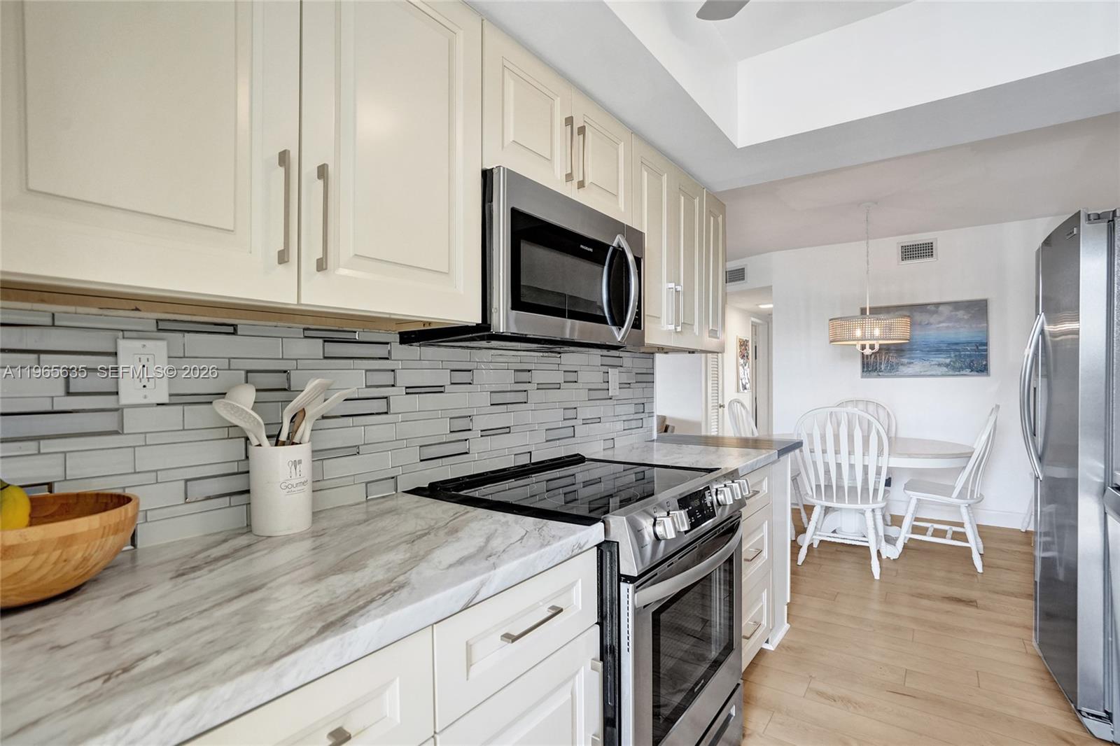 A kitchen features cream cabinets, a patterned tile backsplash, marble-look countertops, and stainless steel appliances — 934 SE 9th Ave # 17, Pompano Beach FL 33060, POMPANO BEACH, FL