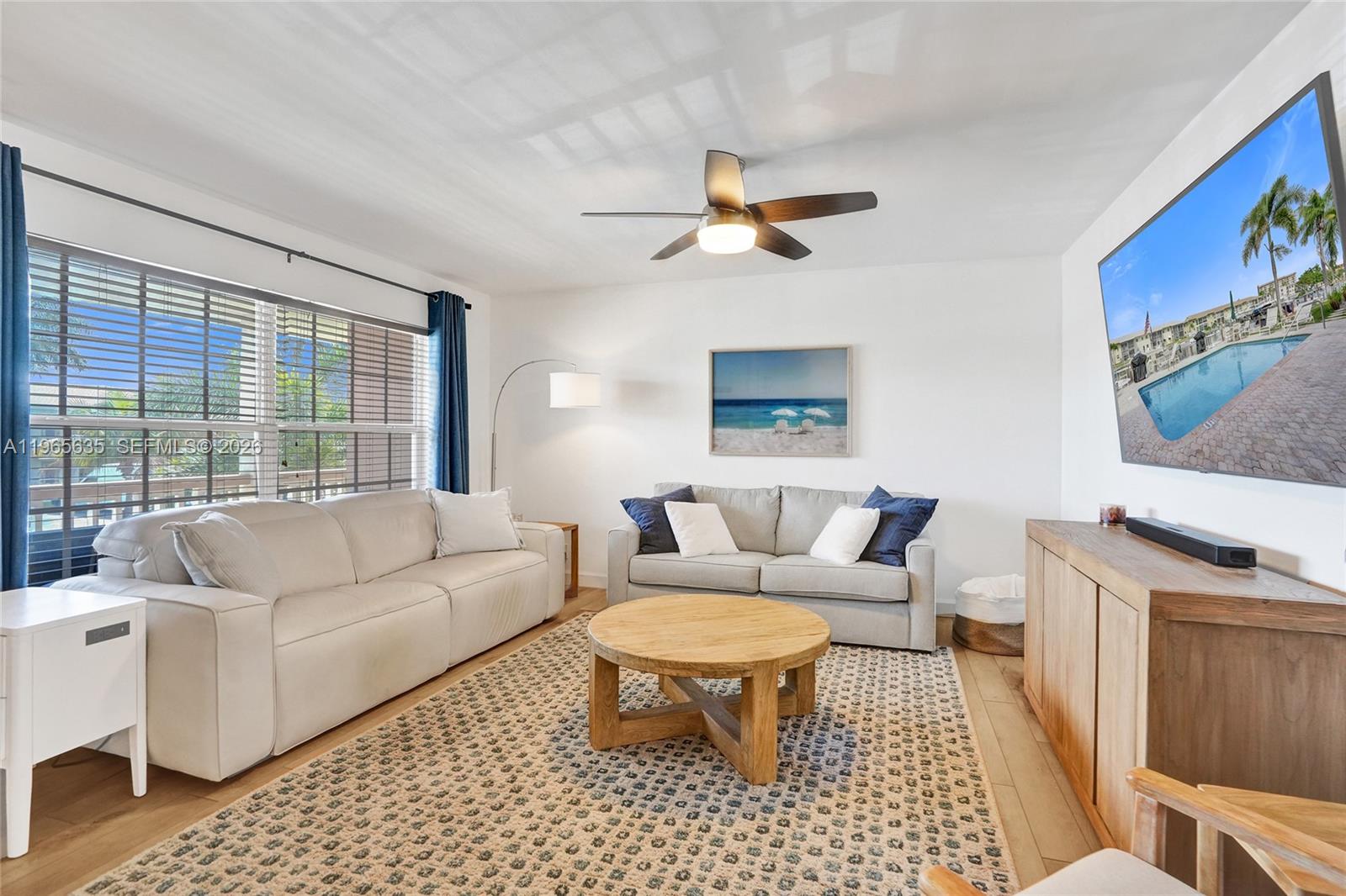 A living room features two sofas, a round wooden coffee table, and a wall-mounted television — 934 SE 9th Ave # 17, Pompano Beach FL 33060, POMPANO BEACH, FL