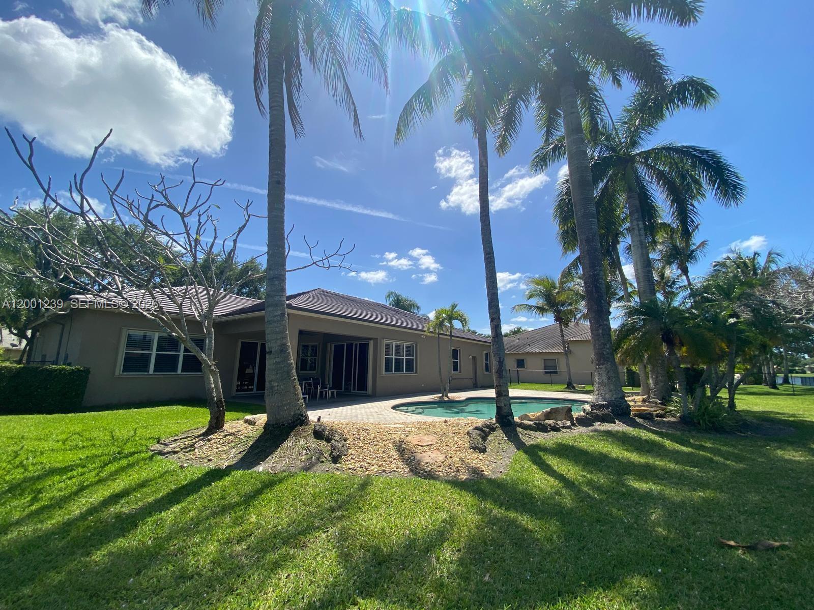 A backyard features a swimming pool, a patio, and several palm trees behind a house — 13805 SW 41st St, Davie FL 33330, DAVIE, FL