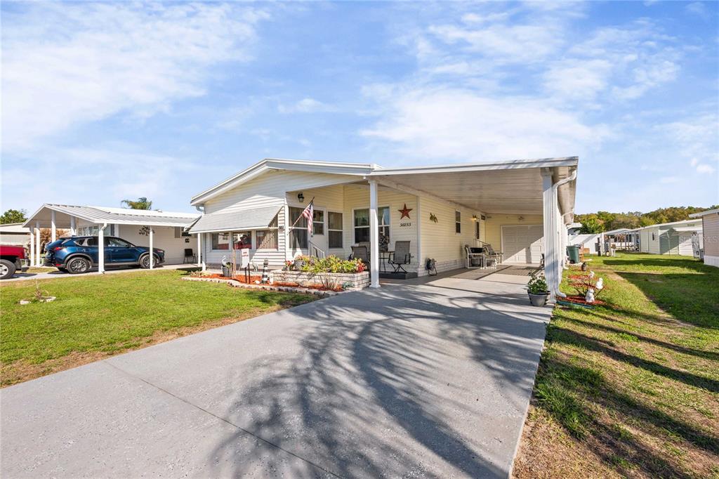 A light-colored manufactured home features a concrete driveway, a carport, and a small front porch — 36853 JODI AVENUE, ZEPHYRHILLS, FL