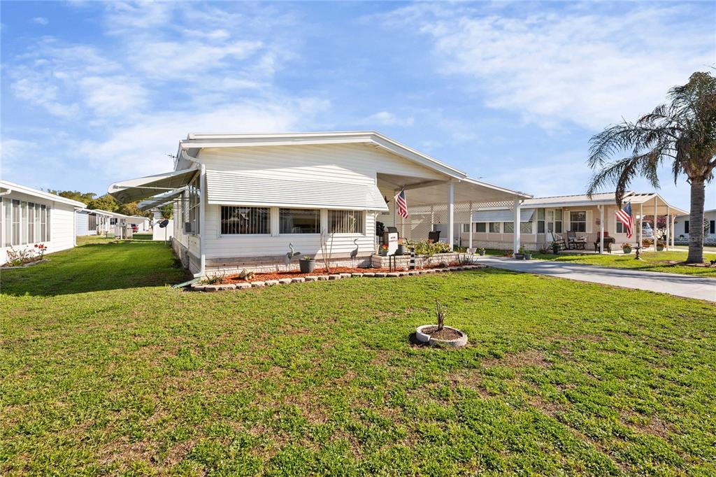 A white mobile home with a covered carport and a grassy front yard — 36853 JODI AVENUE, ZEPHYRHILLS, FL
