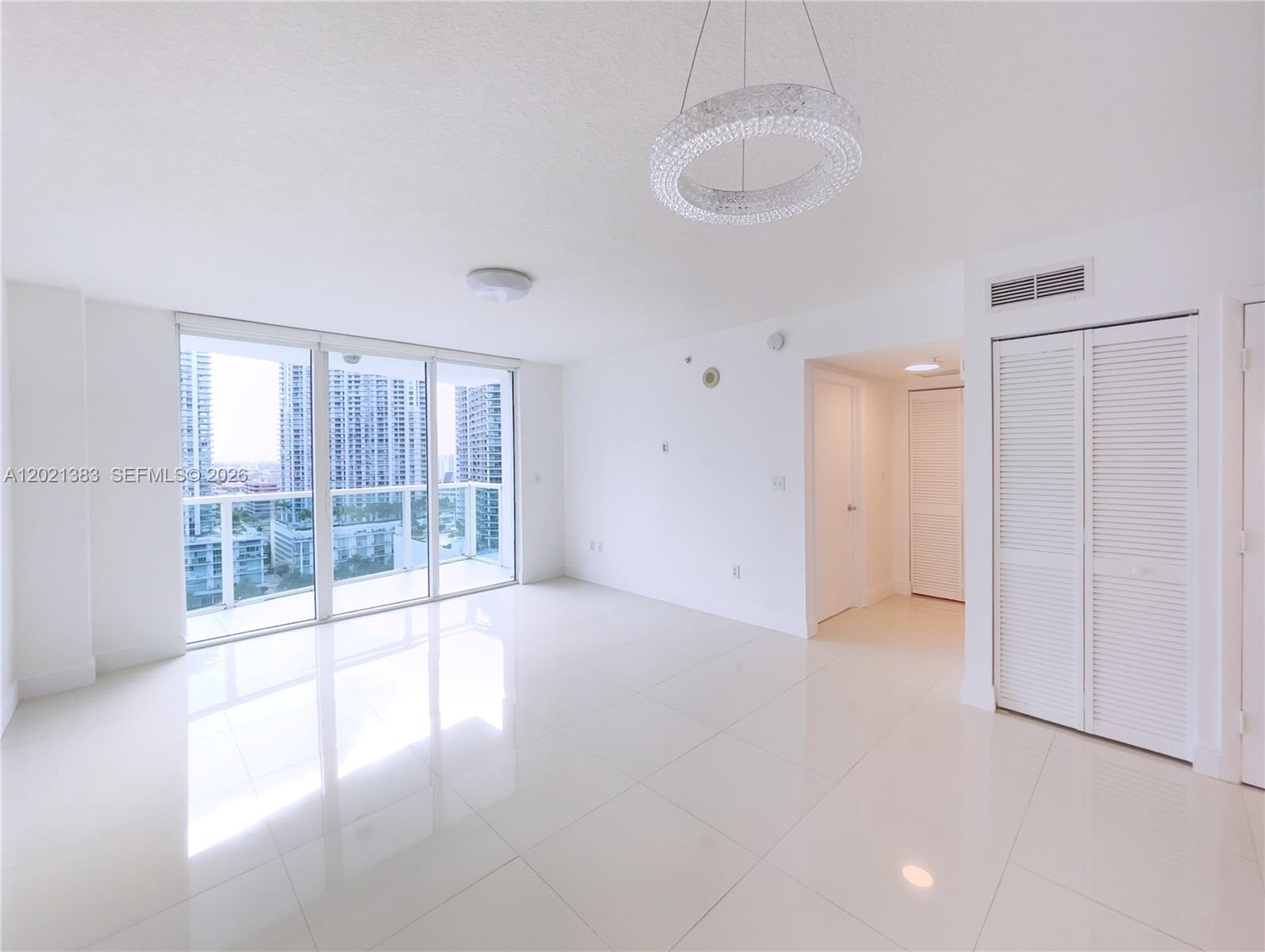 A bright, empty living room features white tile floors, a modern chandelier, and a balcony — 31 SE 5th St # 2307, Miami FL 33131, MIAMI, FL