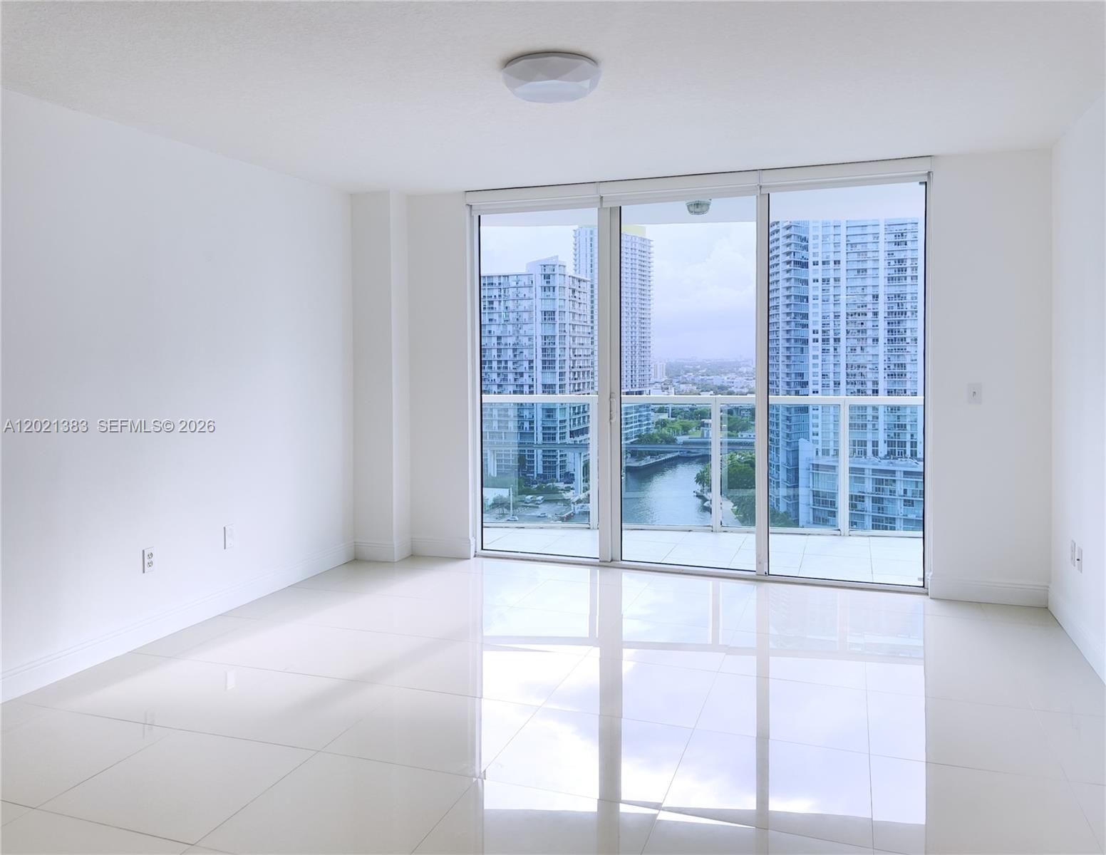 An empty room with white tile floors and a sliding glass door overlooking city buildings — 31 SE 5th St # 2307, Miami FL 33131, MIAMI, FL