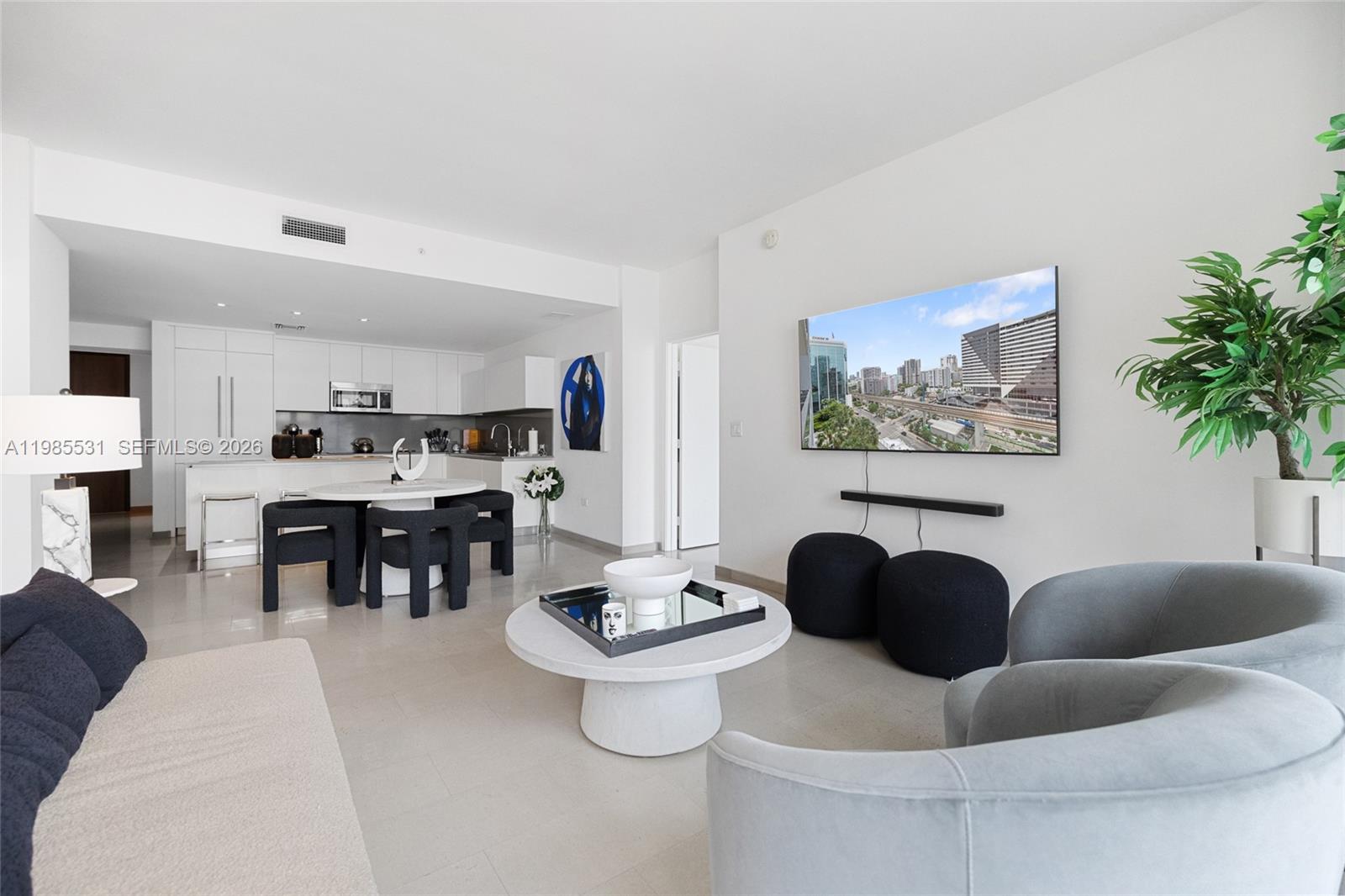 A modern living room and kitchen area feature white cabinetry, light tile floors, and furniture — 88 SW 7th St # 1010, Miami FL 33130, MIAMI, FL
