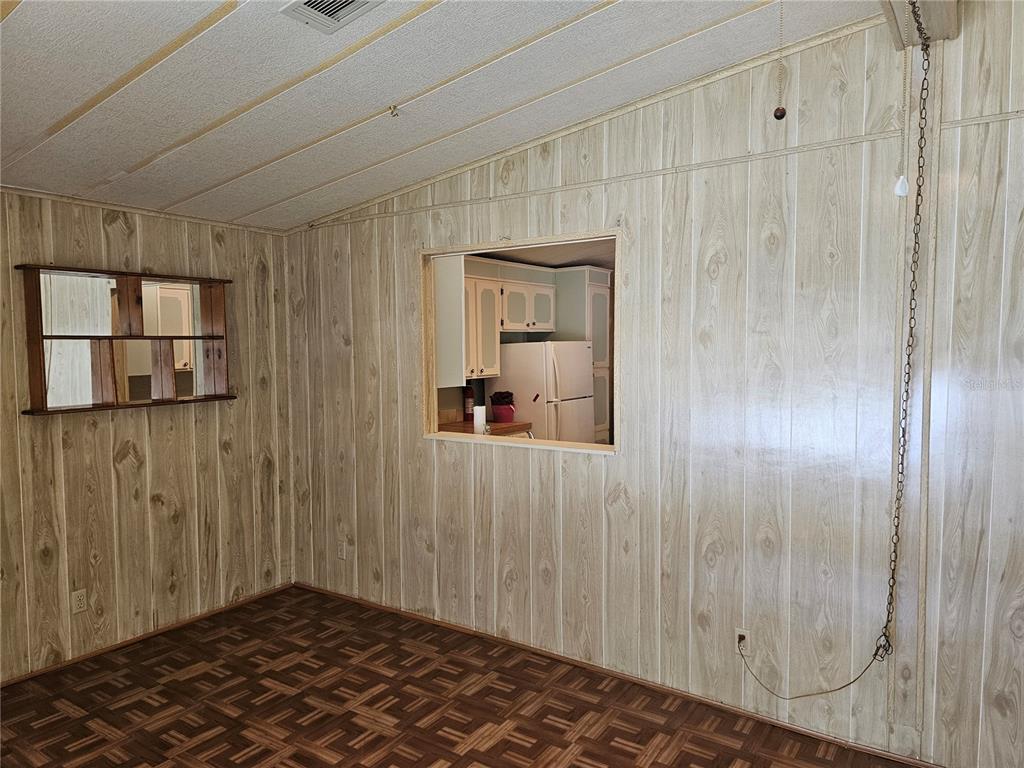 A room with wood-paneled walls, a pass-through window to the kitchen, and parquet flooring — 198 SUNSET DRIVE, LAKE ALFRED, FL
