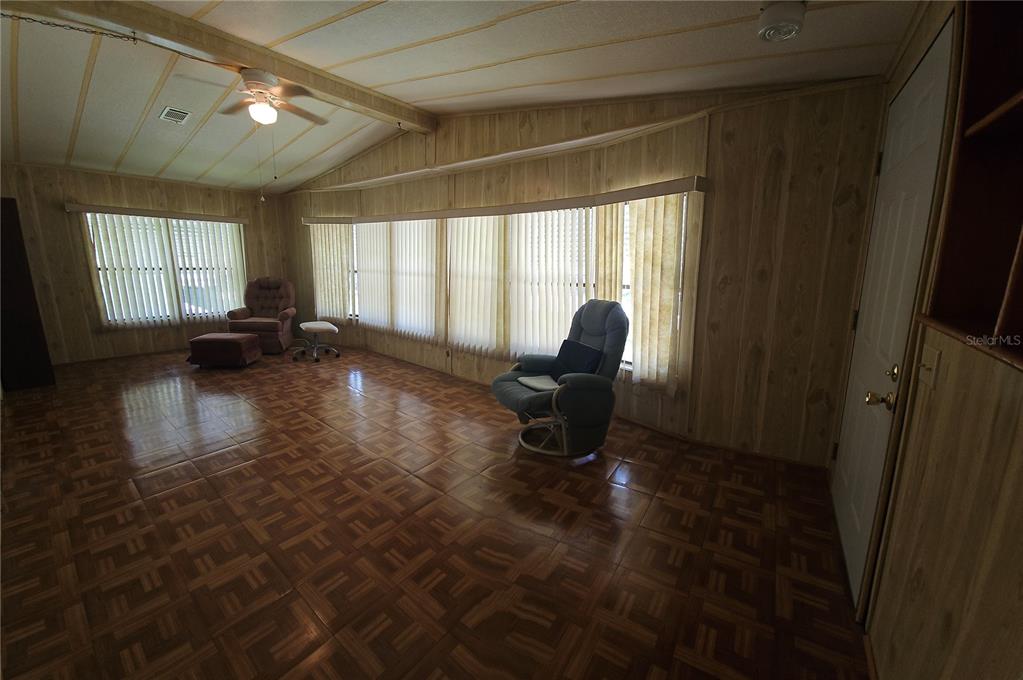 A living room features wood-paneled walls, tiled flooring, a ceiling fan, and large windows with blinds — 198 SUNSET DRIVE, LAKE ALFRED, FL