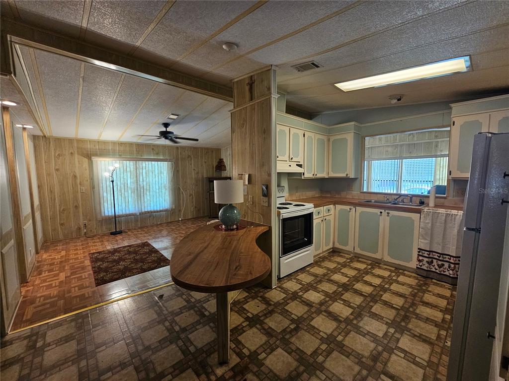 A kitchen with wood-paneled walls, a breakfast bar, and checkered flooring opens to a living area — 198 SUNSET DRIVE, LAKE ALFRED, FL