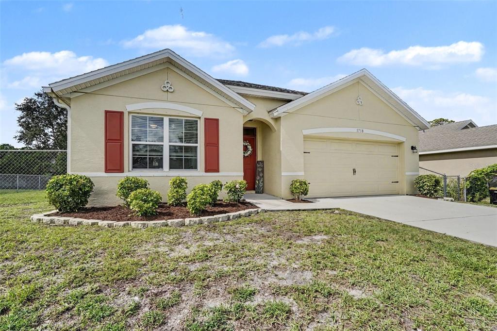 A single-story house features a tan stucco exterior, red shutters, and a two-car garage — 1718 PACE DR NW, PALM BAY, FL