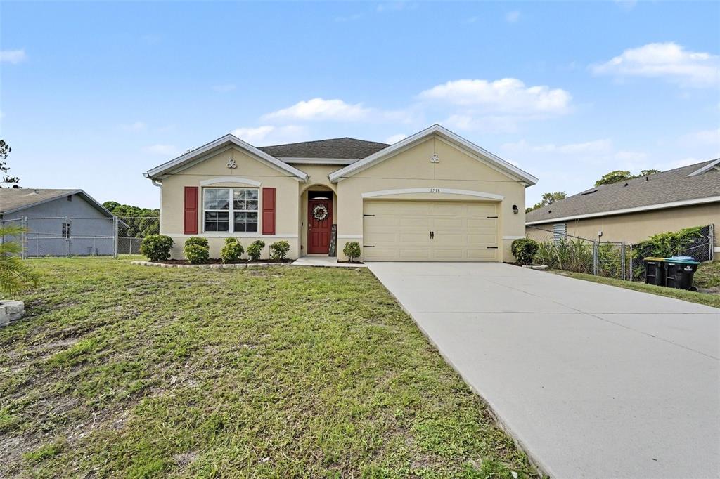 A single-story house with beige stucco siding, a two-car garage, and red window shutters — 1718 PACE DR NW, PALM BAY, FL