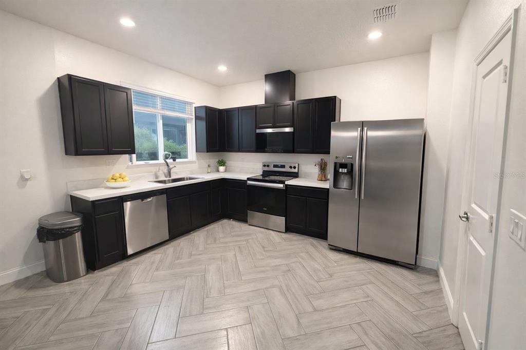 A kitchen features black cabinets, stainless steel appliances, white countertops, and light-colored herringbone tile flooring — 3678 GRAPPLER CIRCLE SE, PALM BAY, FL