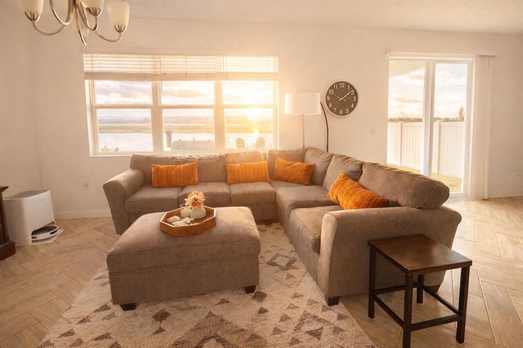 A living room features a large sectional sofa, an ottoman, and windows overlooking a lake — 3678 GRAPPLER CIRCLE SE, PALM BAY, FL