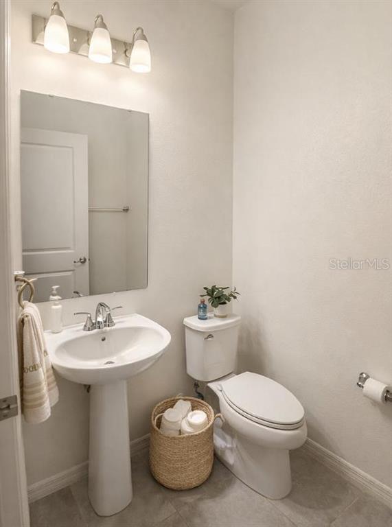A small bathroom features a pedestal sink, a white toilet, and a wall-mounted mirror — 3678 GRAPPLER CIRCLE SE, PALM BAY, FL