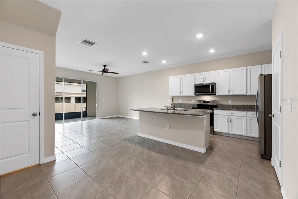 An open-concept kitchen with white cabinets, granite countertops, and tile flooring leads to a patio — 3507 MARIGOLD PATCH COURT, PLANT CITY, FL