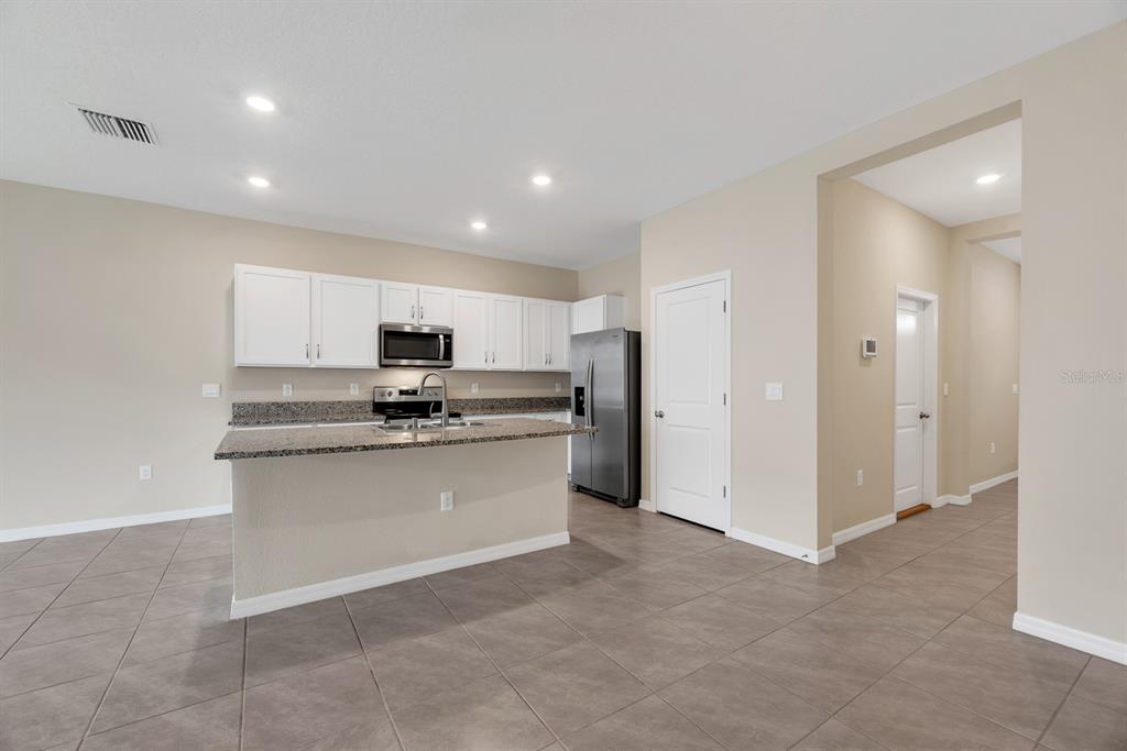 A kitchen features white cabinets, granite countertops, a stainless steel refrigerator, and tile flooring — 3507 MARIGOLD PATCH COURT, PLANT CITY, FL