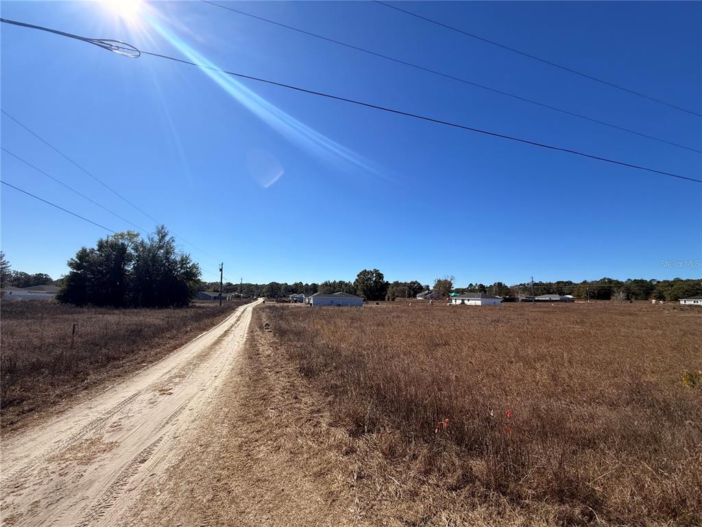 A dirt road runs alongside a large, dry grassy field under a clear blue sky — 000 SW 150TH COURT, OCALA, FL