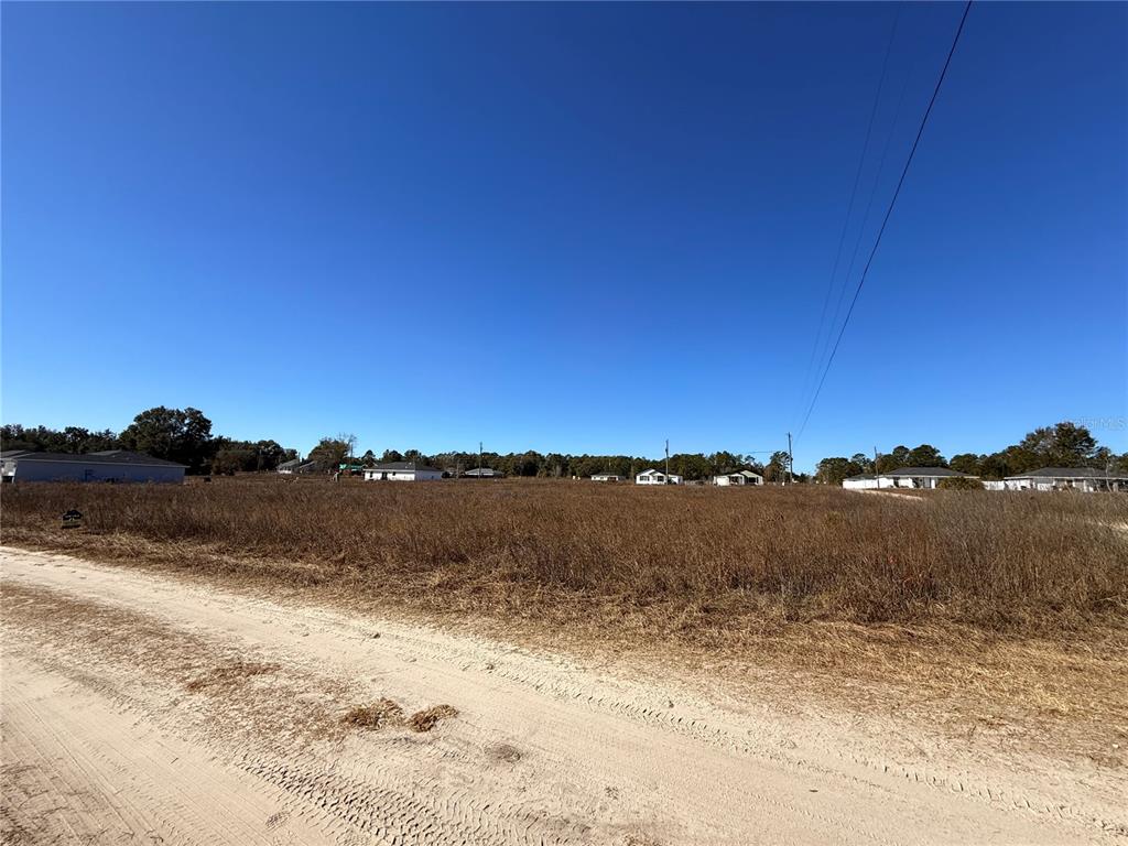 A dirt road runs alongside a large, flat, undeveloped grassy lot under a clear sky — 000 SW 150TH COURT, OCALA, FL