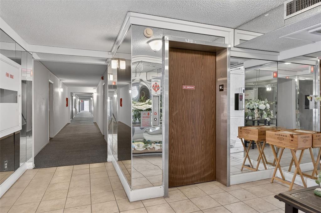 An elevator with a wood door sits in a tiled hallway with mirrored wall panels — 519 ALBEE FARM ROAD UNIT 214, VENICE, FL