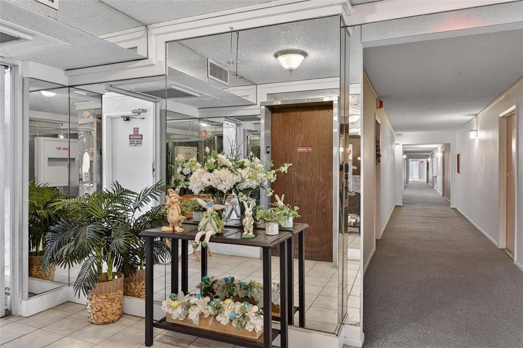 A hallway features a mirrored wall, a console table with Easter decor, and potted plants — 519 ALBEE FARM ROAD UNIT 214, VENICE, FL