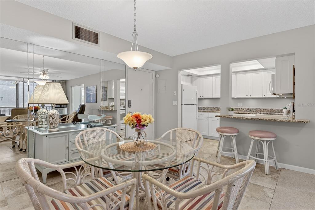 A dining area with a glass table and rattan chairs sits adjacent to a kitchen bar — 519 ALBEE FARM ROAD UNIT 214, VENICE, FL