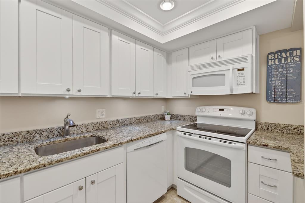 A kitchen features white cabinets, granite countertops, a stainless steel sink, and white appliances — 519 ALBEE FARM ROAD UNIT 214, VENICE, FL