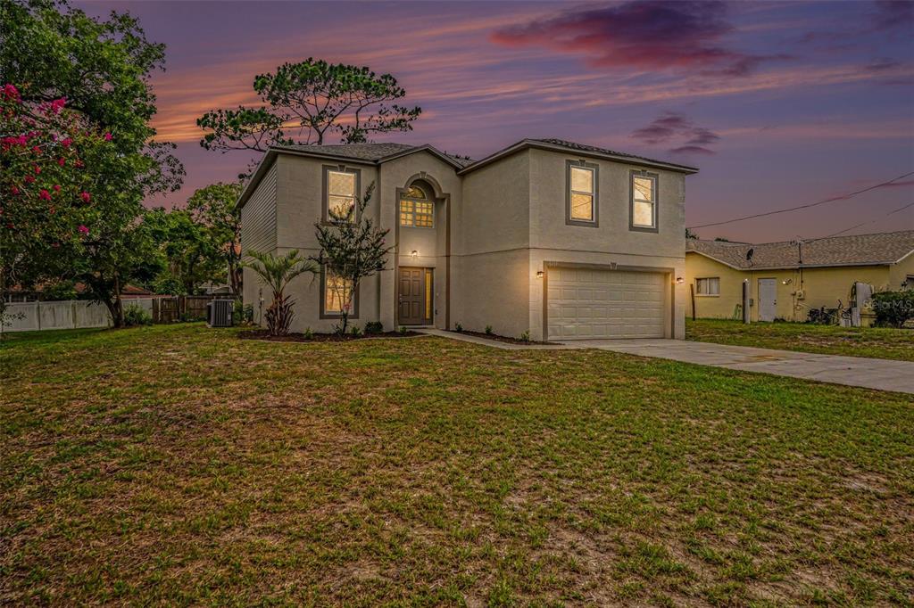 A two-story beige house with a two-car garage sits on a grassy lot — 6197 HELMLY AVENUE, SPRING HILL, FL