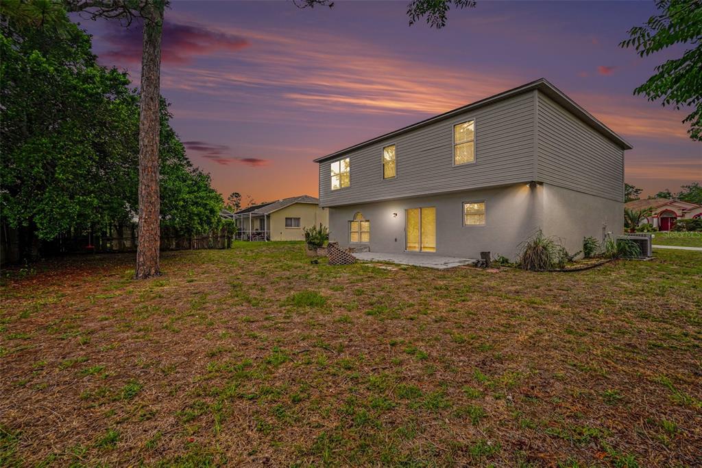 The exterior rear view of a two-story house with a small patio and grassy yard — 6197 HELMLY AVENUE, SPRING HILL, FL