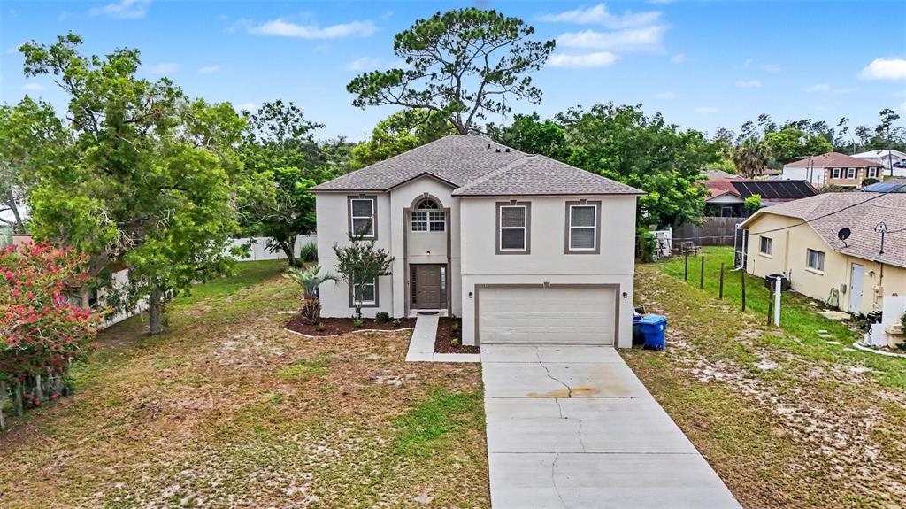 A two-story house with a beige stucco exterior, a concrete driveway, and a shingled roof — 6197 HELMLY AVENUE, SPRING HILL, FL