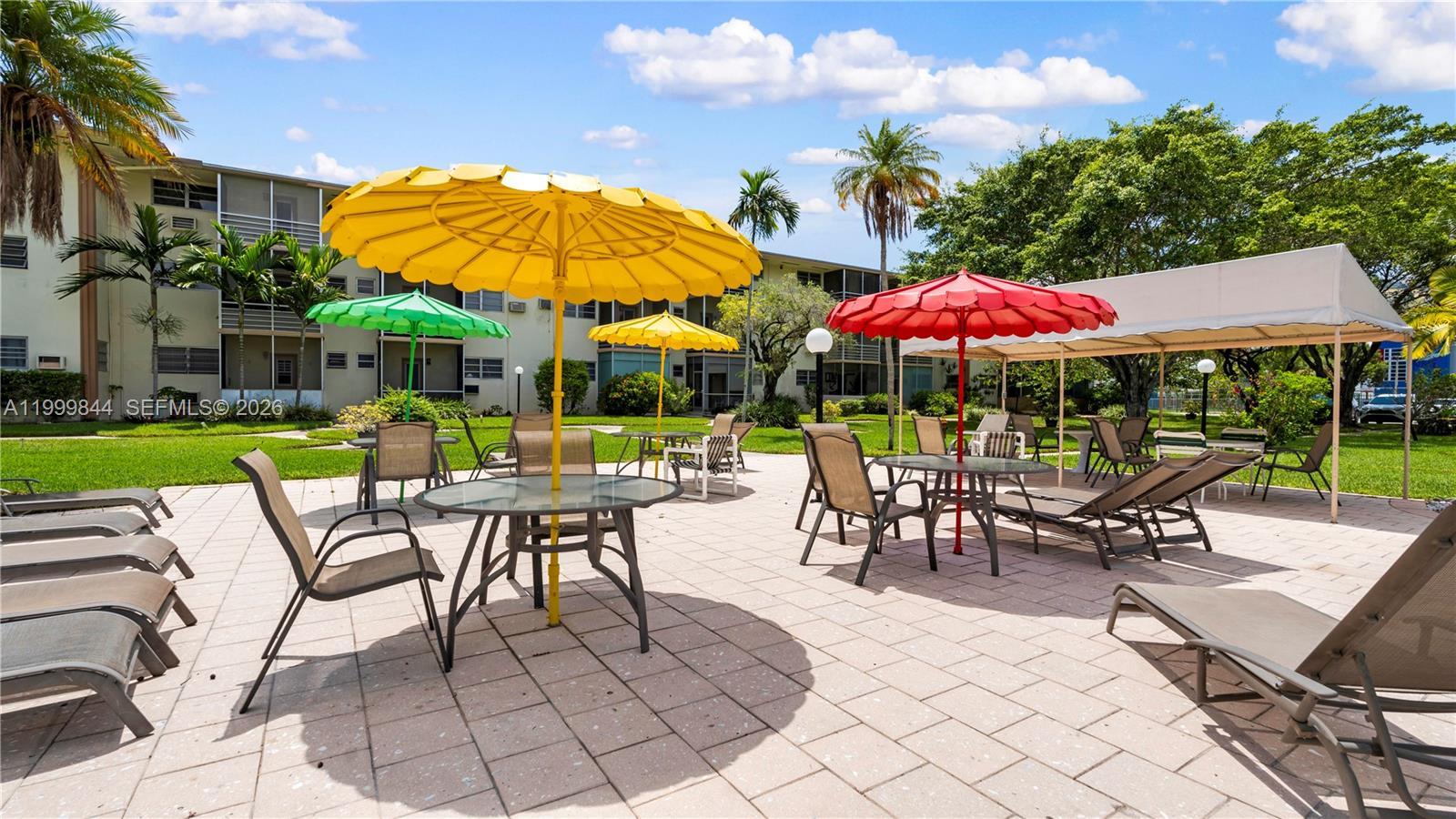 A paved patio area features multiple tables with colorful umbrellas and lounge chairs near apartments — 16900 NE 14th Ave # 204, Miami FL 33162, MIAMI, FL