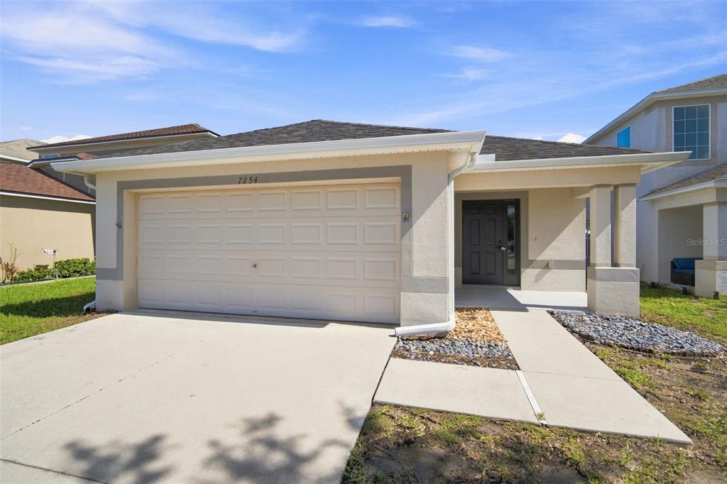 A single-story house with a beige stucco exterior, a two-car garage, and a covered entryway — 7254 LUMBER PORT DRIVE, RUSKIN, FL