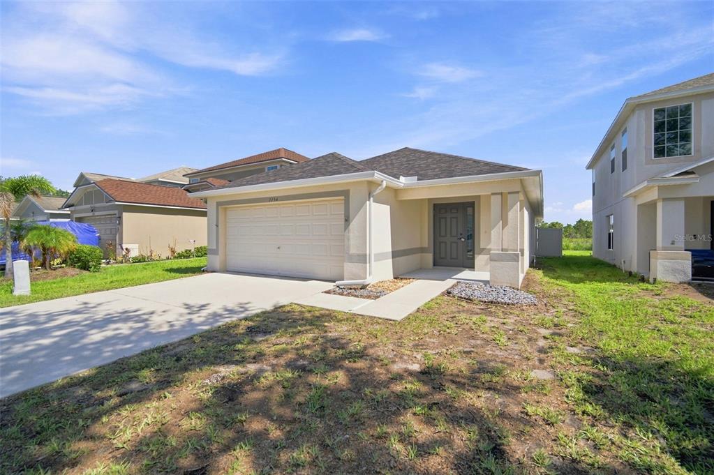 A single-story house with a beige stucco exterior, a two-car garage, and a gray door — 7254 LUMBER PORT DRIVE, RUSKIN, FL