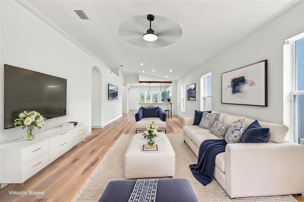 A living room with white walls, wood-look flooring, a large television, and blue-accented furniture — 7254 LUMBER PORT DRIVE, RUSKIN, FL