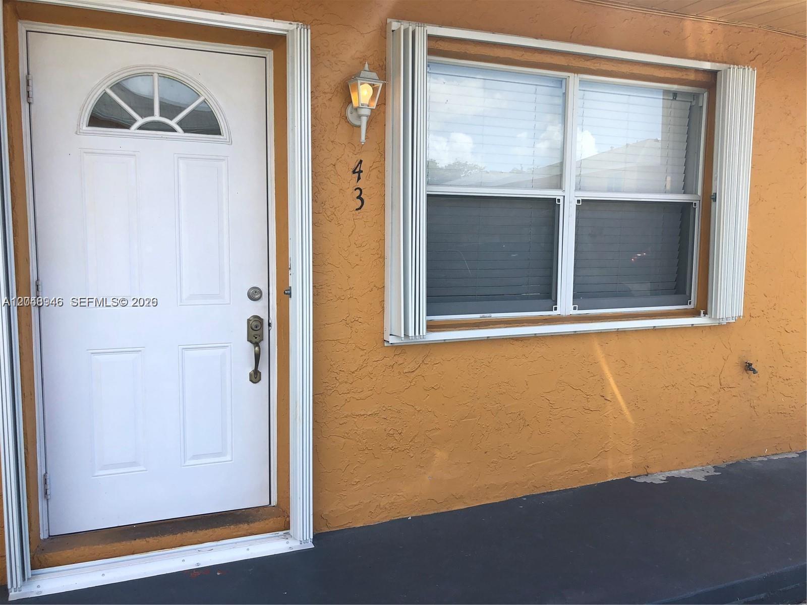 The exterior of a home features an orange stucco wall, a white door, and windows — 43 NE 12th Ave # 43, Homestead FL 33030, HOMESTEAD, FL