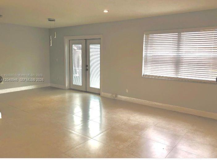 An empty room features light-colored tile flooring, a large window with blinds, and glass-paned doors — 43 NE 12th Ave # 43, Homestead FL 33030, HOMESTEAD, FL