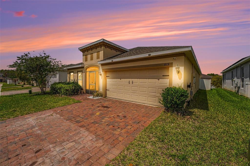 A single-story house with a brick driveway, a two-car garage, and a sunset sky — 815 MONTGOMERY WAY, DAVENPORT, FL