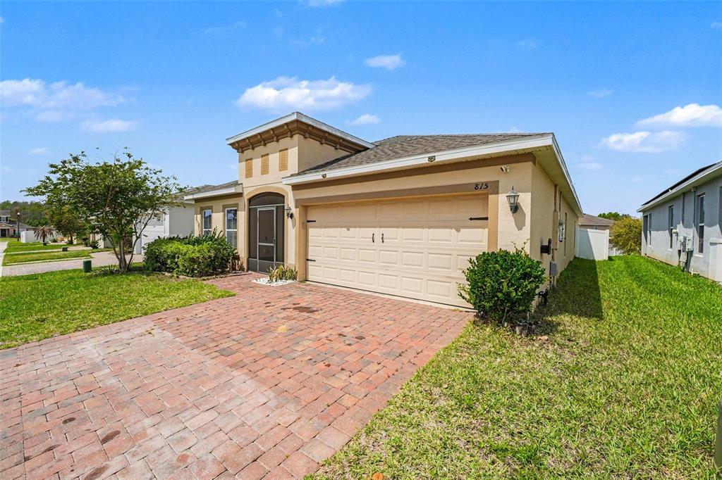 A single-story house with a beige stucco exterior, a brick driveway, and a two-car garage — 815 MONTGOMERY WAY, DAVENPORT, FL