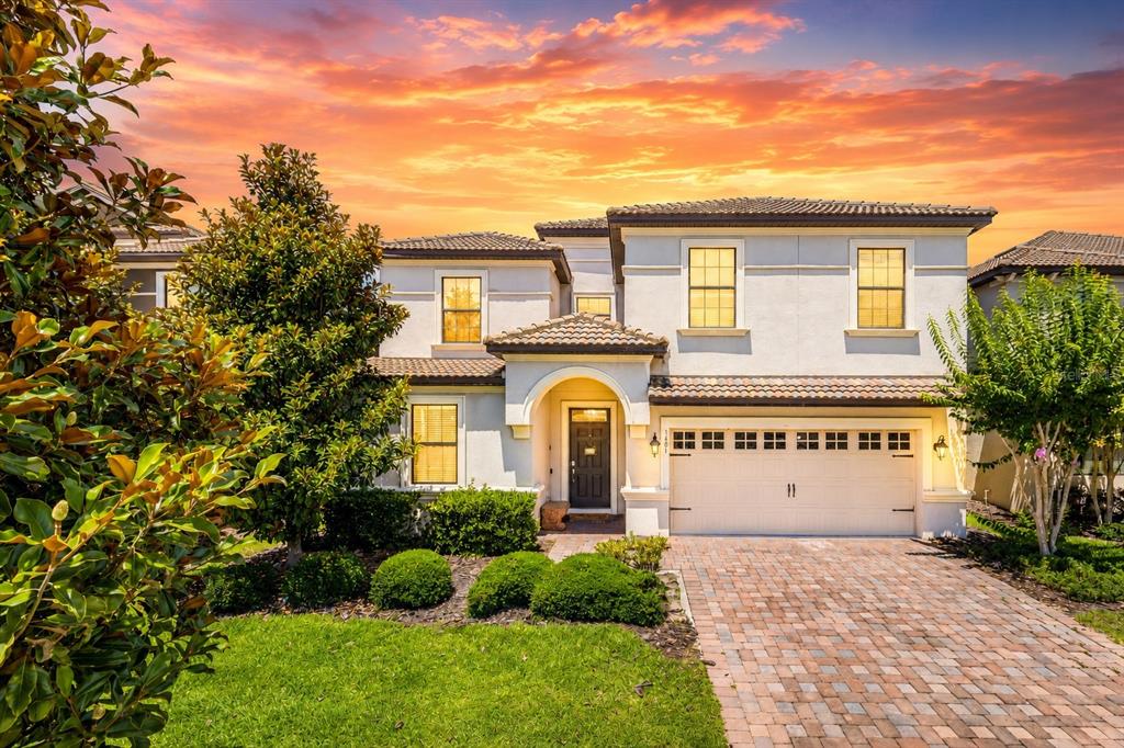 A two-story suburban house with a stucco exterior, tile roof, and a brick paver driveway — 1406 WEXFORD WAY, DAVENPORT, FL