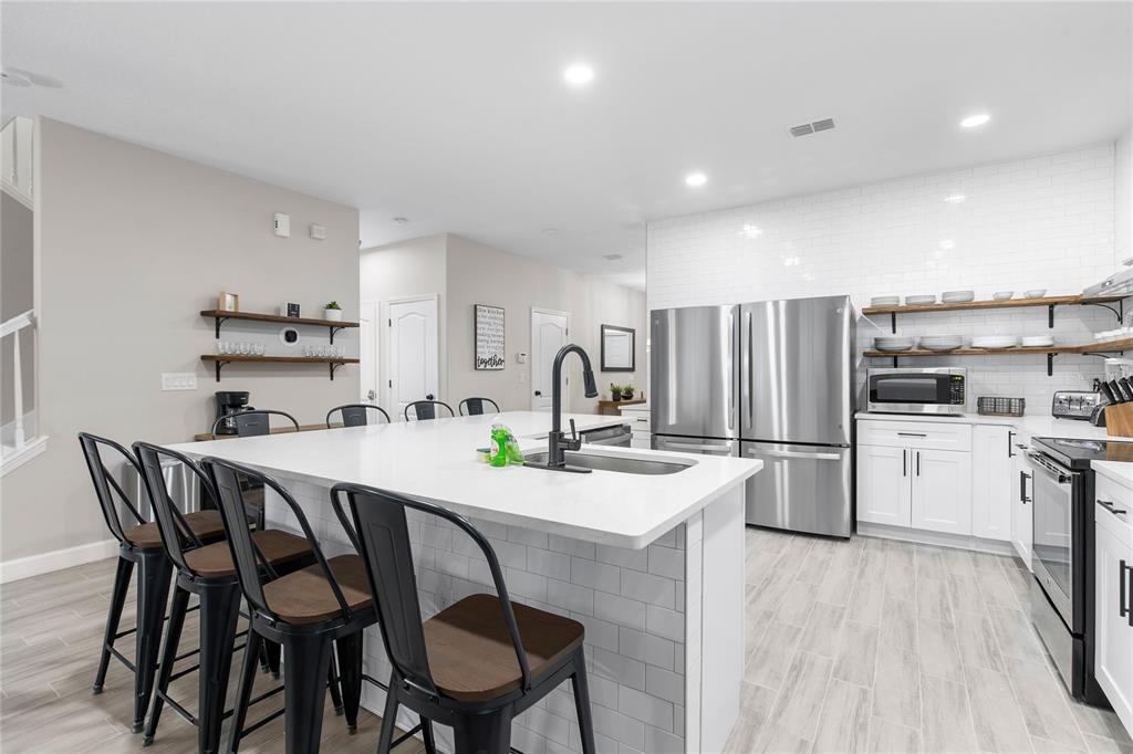 A modern kitchen features a white quartz island, stainless steel appliances, and open wood shelving — 1406 WEXFORD WAY, DAVENPORT, FL