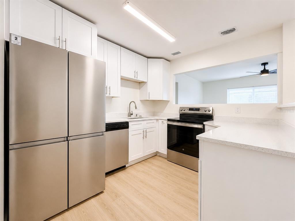 A kitchen features white cabinets, stainless steel appliances, and light wood-look flooring — 4112 OHIO AVENUE, TAMPA, FL