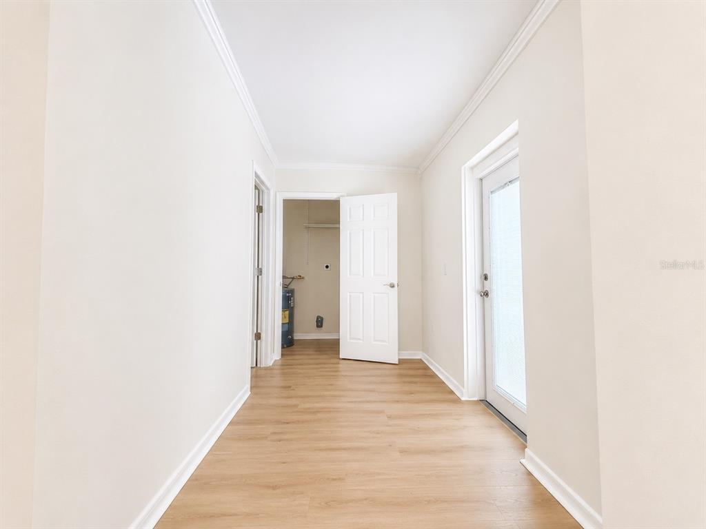 A hallway with light wood-look flooring leads to a utility room and an exterior door — 4112 OHIO AVENUE, TAMPA, FL