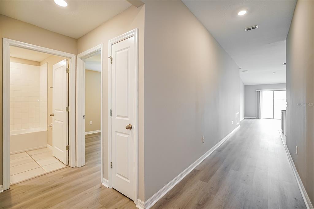 A hallway with light wood-look flooring leads to a living area with sliding glass doors — 12495 SE 100TH AVENUE, BELLEVIEW, FL