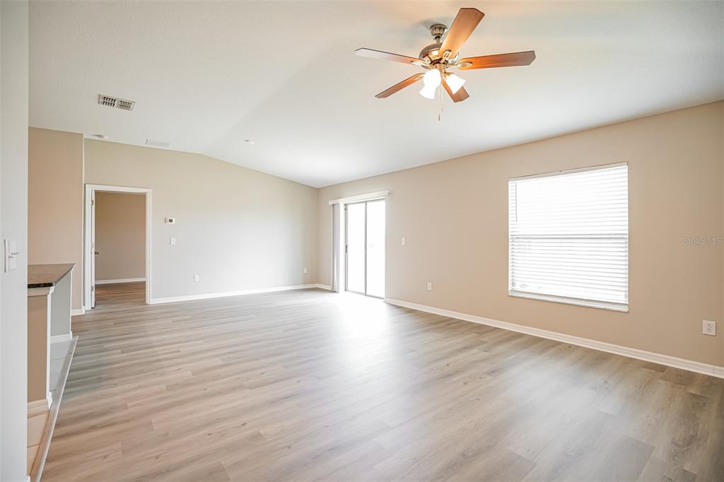 A spacious living room with light wood-look flooring, a ceiling fan, and sliding glass doors — 12495 SE 100TH AVENUE, BELLEVIEW, FL