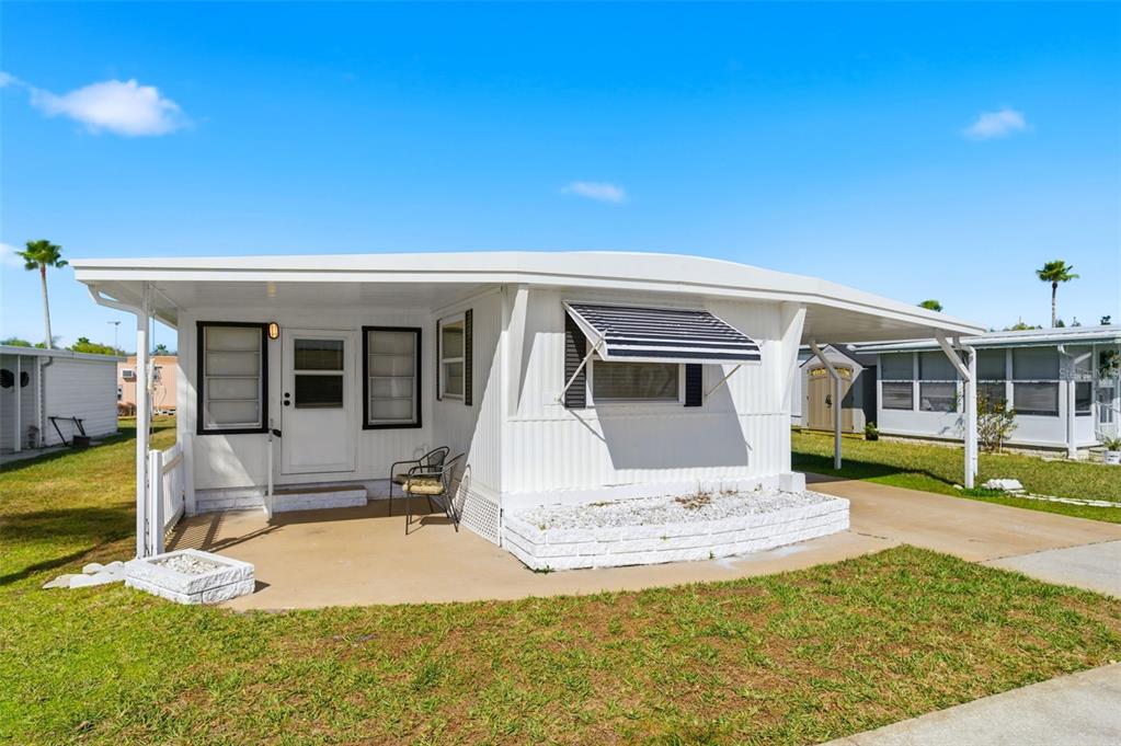 A white mobile home with a carport, a small front patio, and striped window awnings — 10913 LIBERTY DRIVE, PORT RICHEY, FL