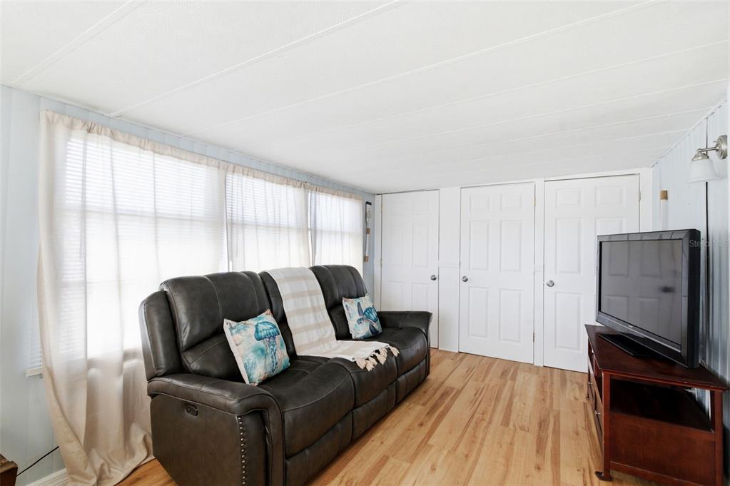 A living room features a dark leather sofa, wood-look flooring, and three white doors — 10913 LIBERTY DRIVE, PORT RICHEY, FL